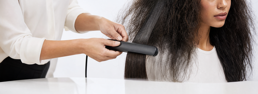 Flat iron, blow dryer with concentrator nozzle, round brush, sectioning clips, and hair care bottles arranged on a salon workstation